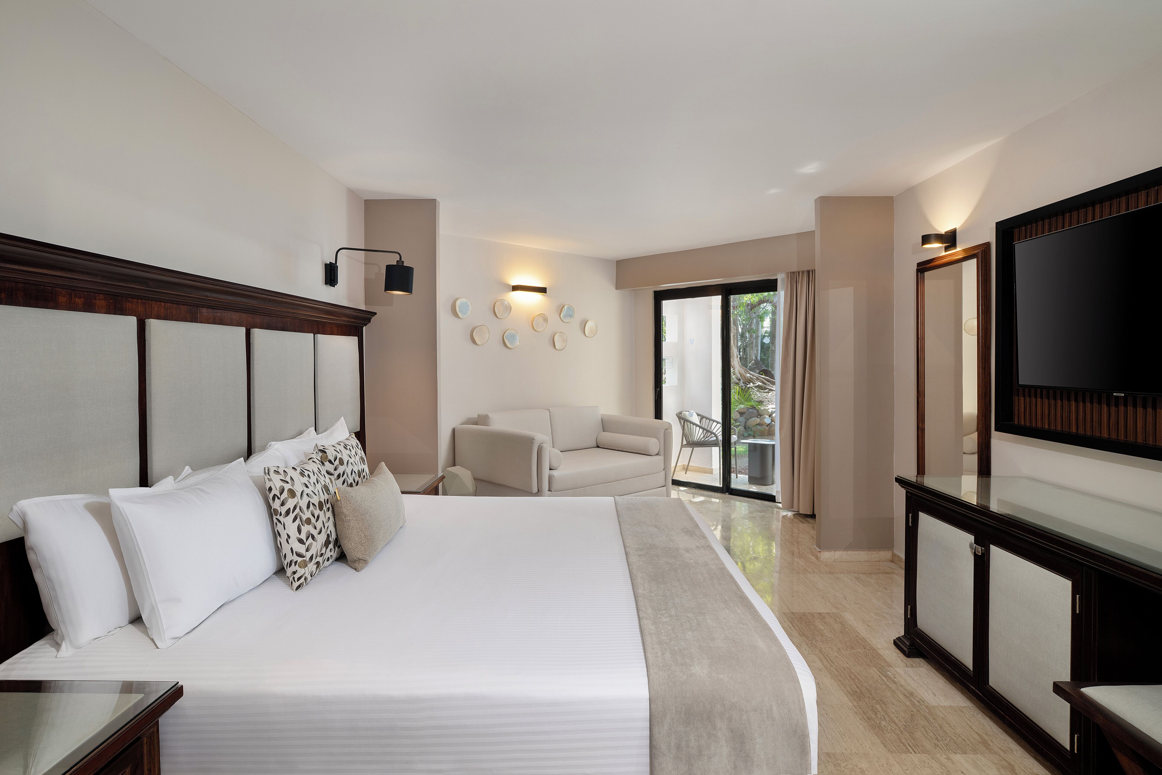 Een hotelkamer met een groot bed, een bank, een televisie en een balkon met uitzicht op bomen.