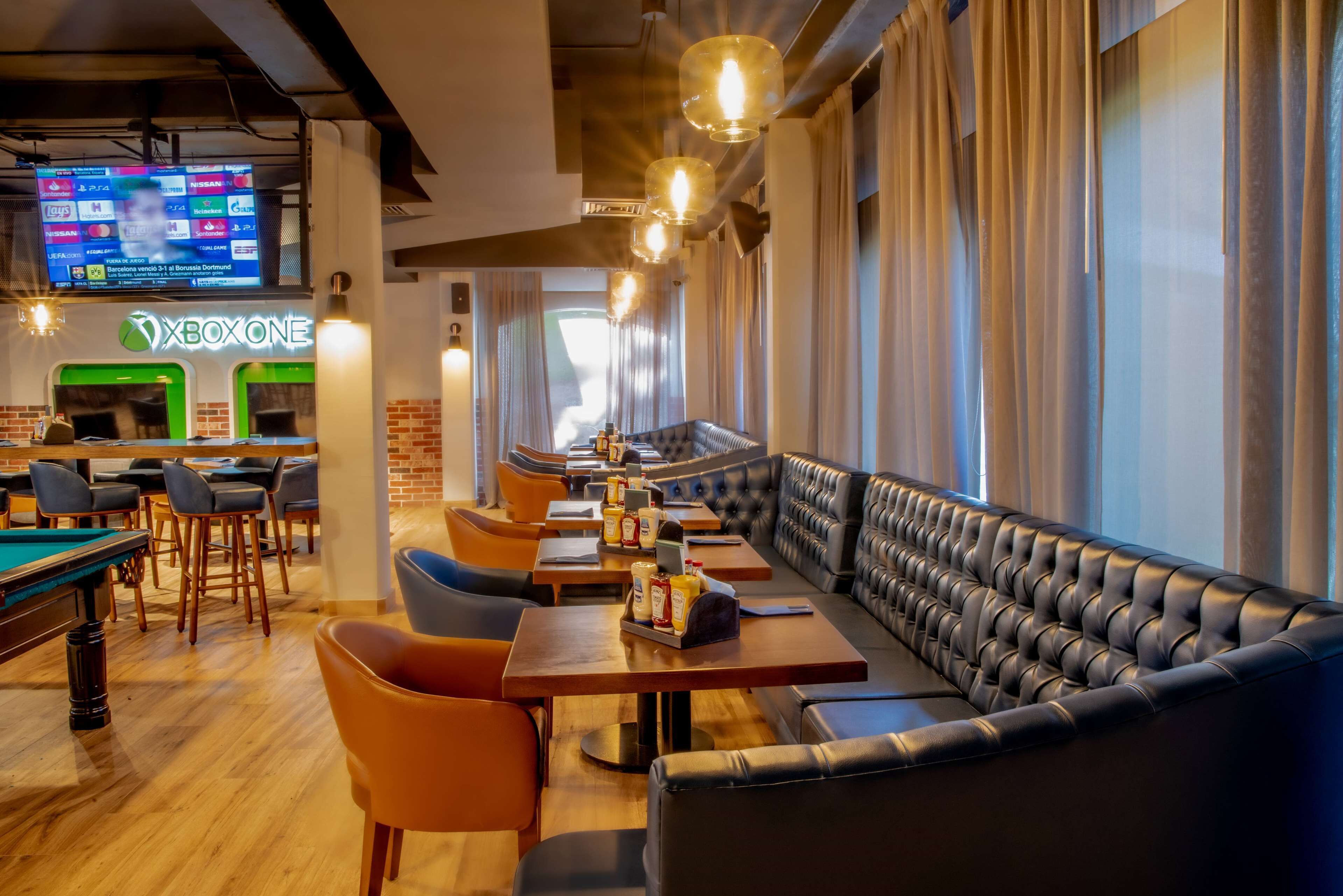 Un área de bar moderna con mesa de billar, asientos de cuero y un letrero de neón para Xbox One.