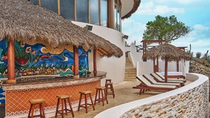 A bar area with a mural, thatched umbrellas, and lounge chairs.