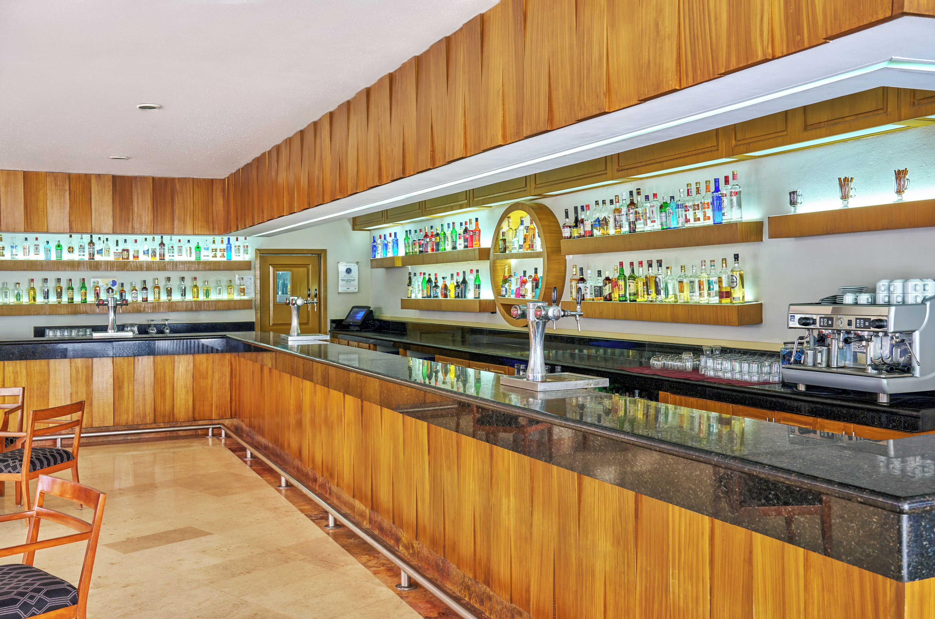 Un espace bar avec des lambris en bois, un long comptoir et des étagères remplies de différentes bouteilles.
