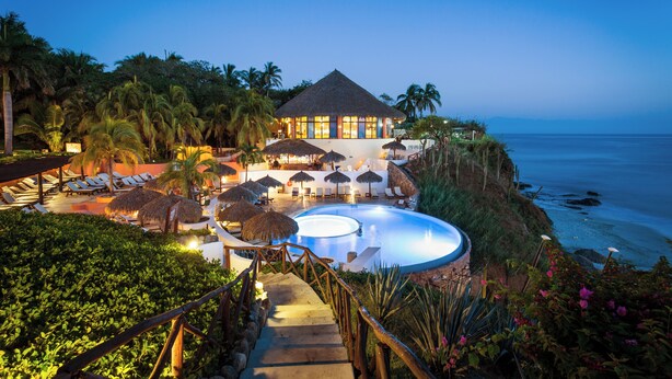 A resort with a swimming pool, lounge chairs, and a view of the ocean.