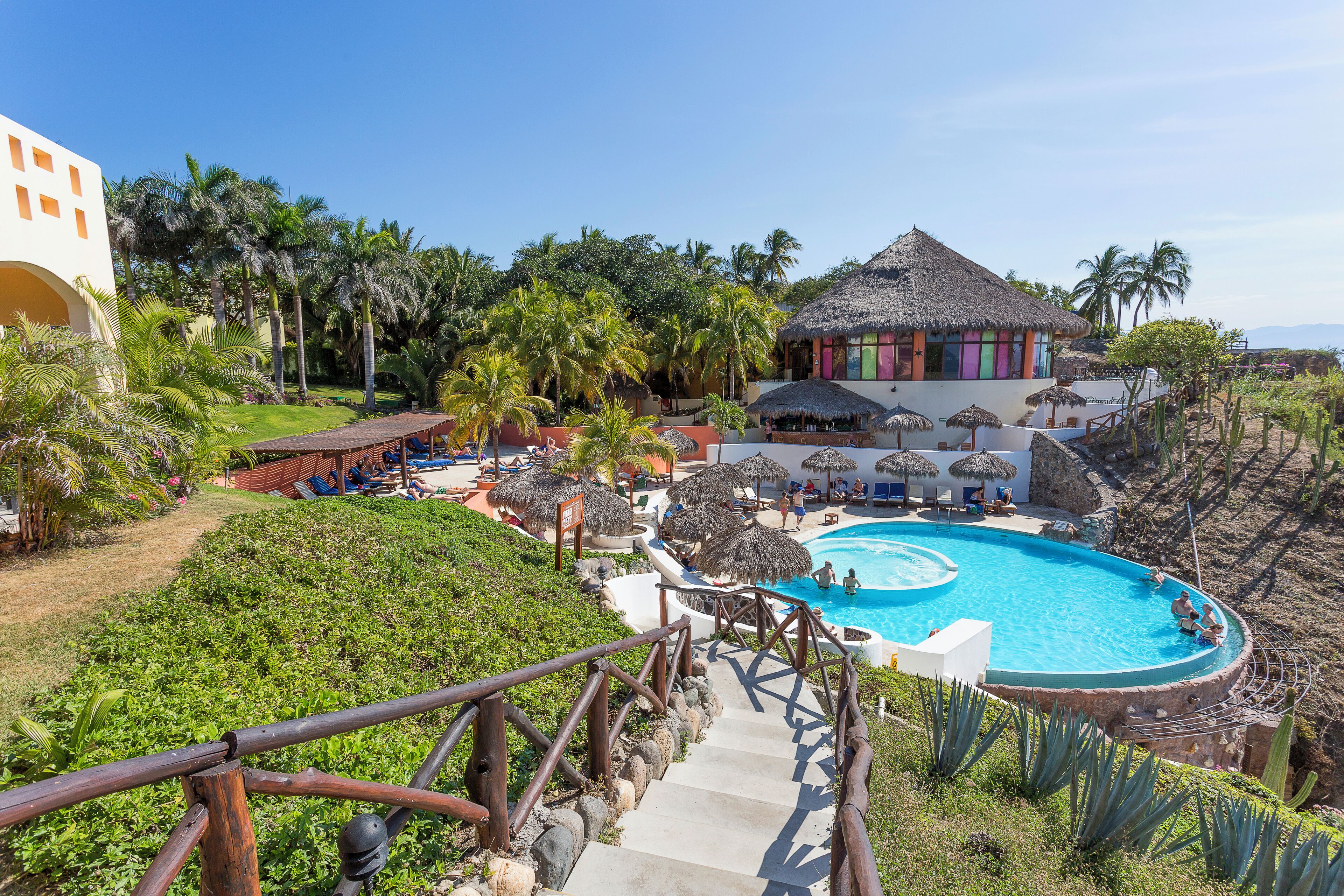 A resort with a swimming pool, palm trees, and a thatched-roof building.