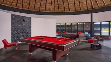 Une table de billard dans une pièce moderne, avec un motif géométrique sur le mur, une chaise rouge et une grande fenêtre portant l’inscription « CLUB ».