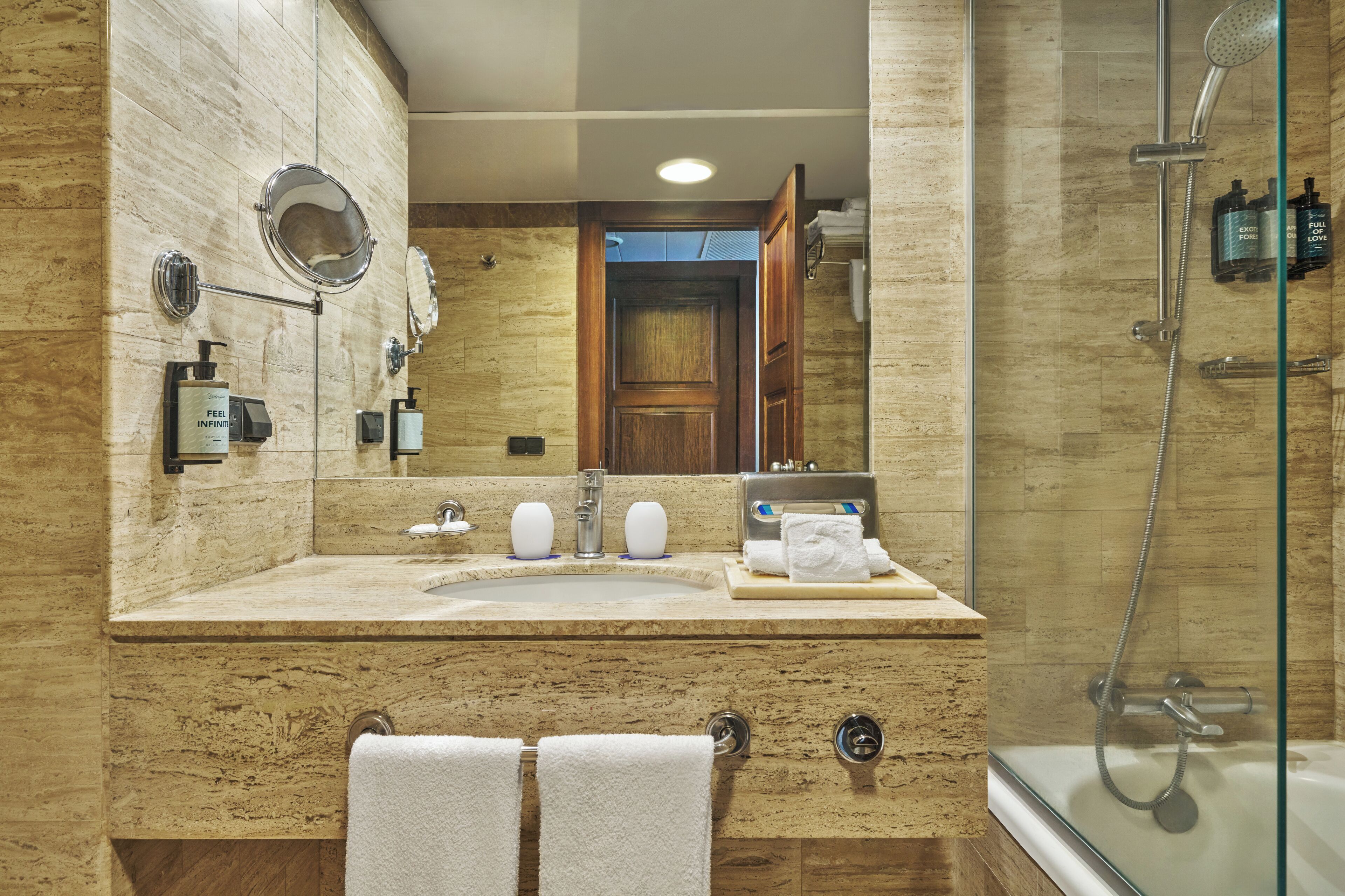 A bathroom with a marble sink, two mirrors, a towel rack, and a glass-enclosed shower area.