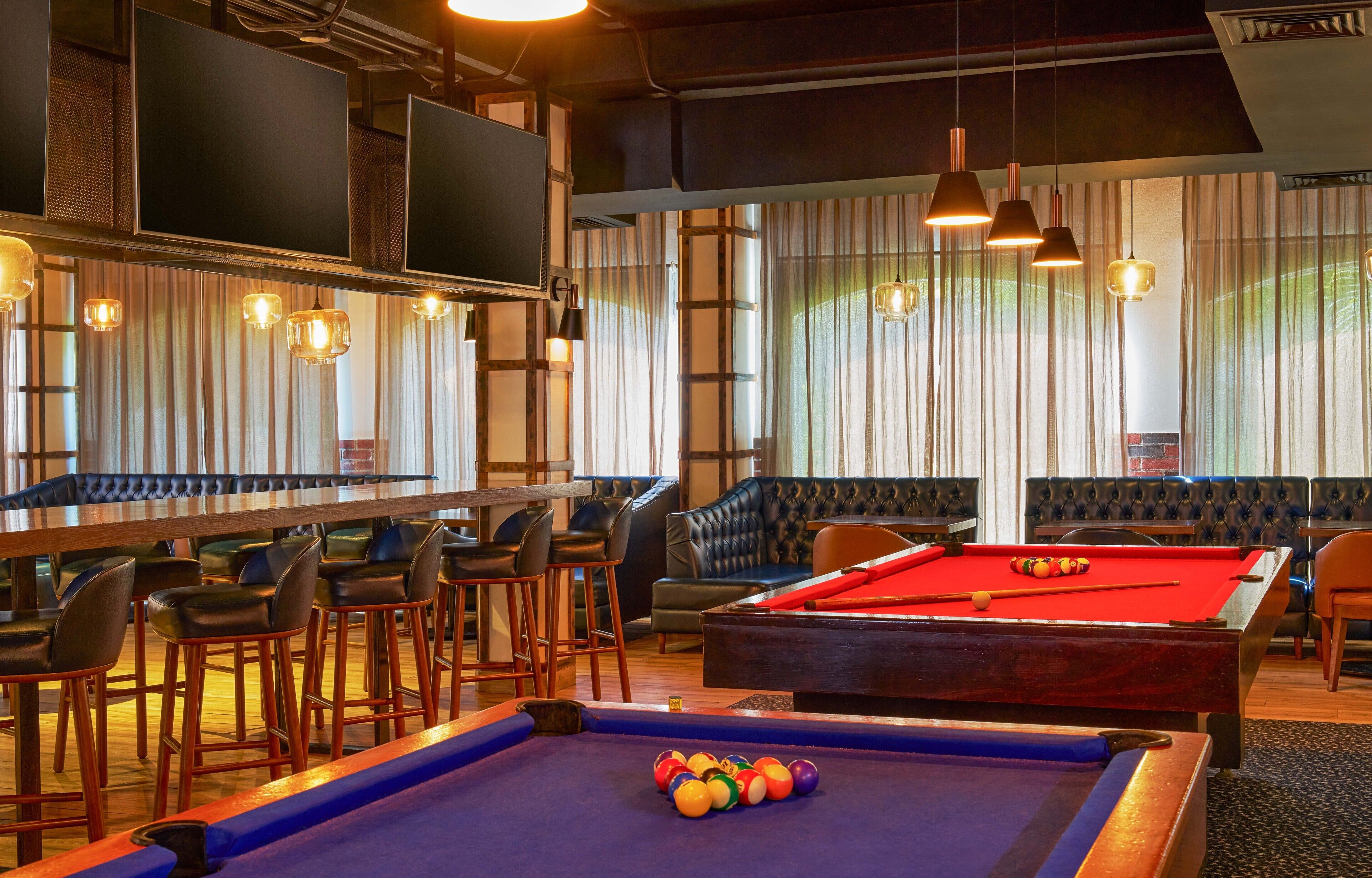 Een biljarttafel met ballen, een bar met krukken en een zithoek met een biljarttafel.