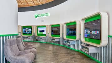 Un espacio de juegos con consolas Xbox One, asientos cómodos y un diseño de pared curva.