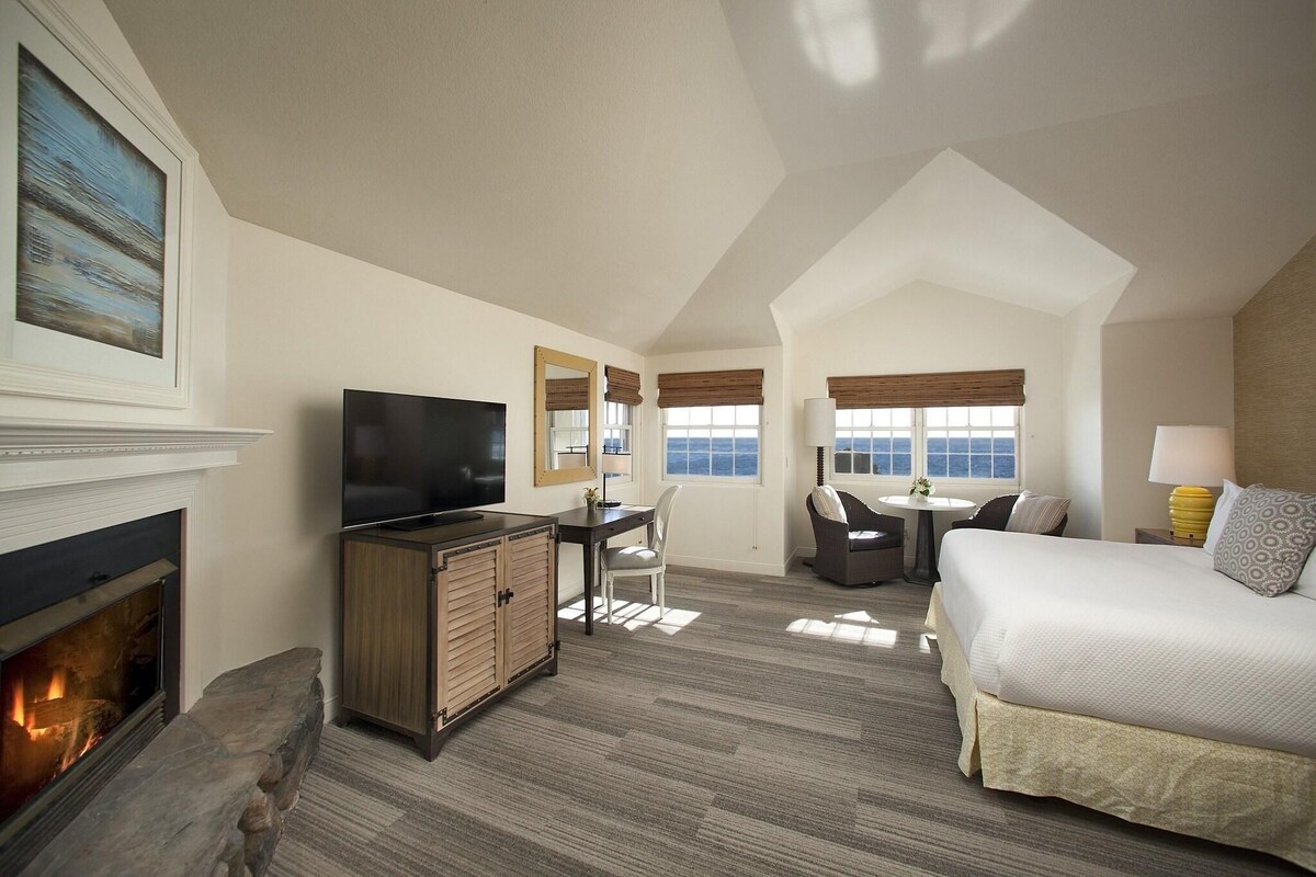 A hotel room with a fireplace, a TV, a desk with a chair, a bed, and a window with a view.