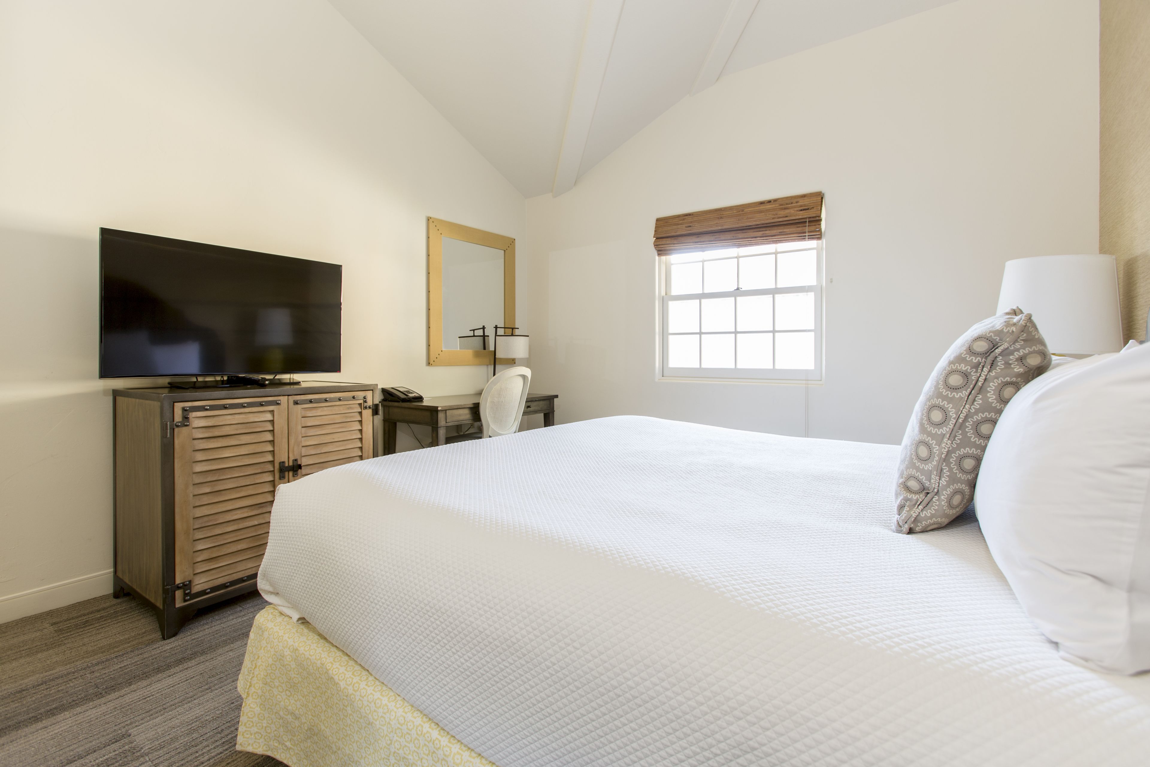Una habitación de hotel con una cama grande, televisión, escritorio y ventana con persianas.