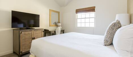 A hotel room with a large bed, a television, a desk, and a window with blinds.