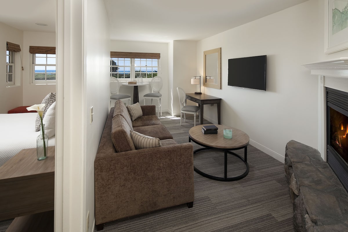 A modern hotel room with a bed, a sofa, a desk, and a fireplace.