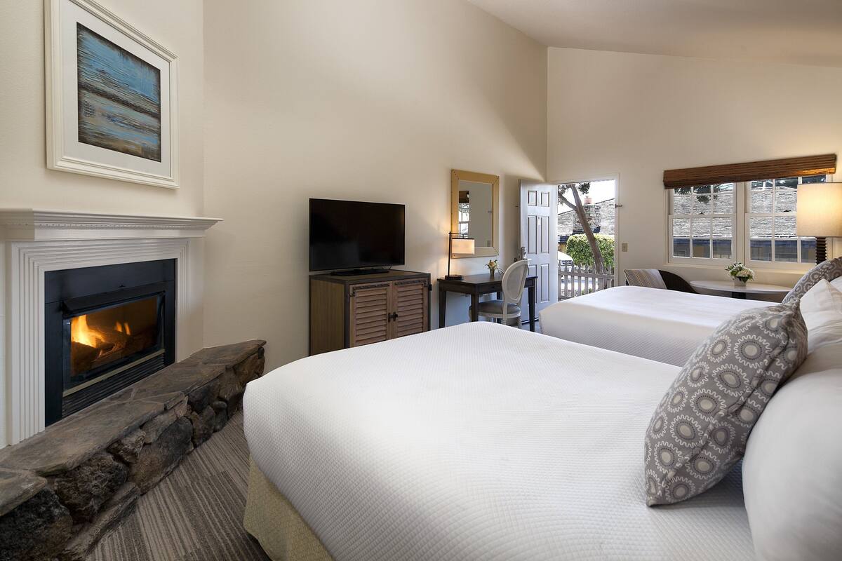 A hotel room with a fireplace, a television, a bed with patterned pillows, and a window with a view.