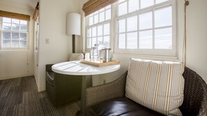 A room with a round table, wicker sofa, and a large window with blinds. - FogCatcher Inn (Cambria)