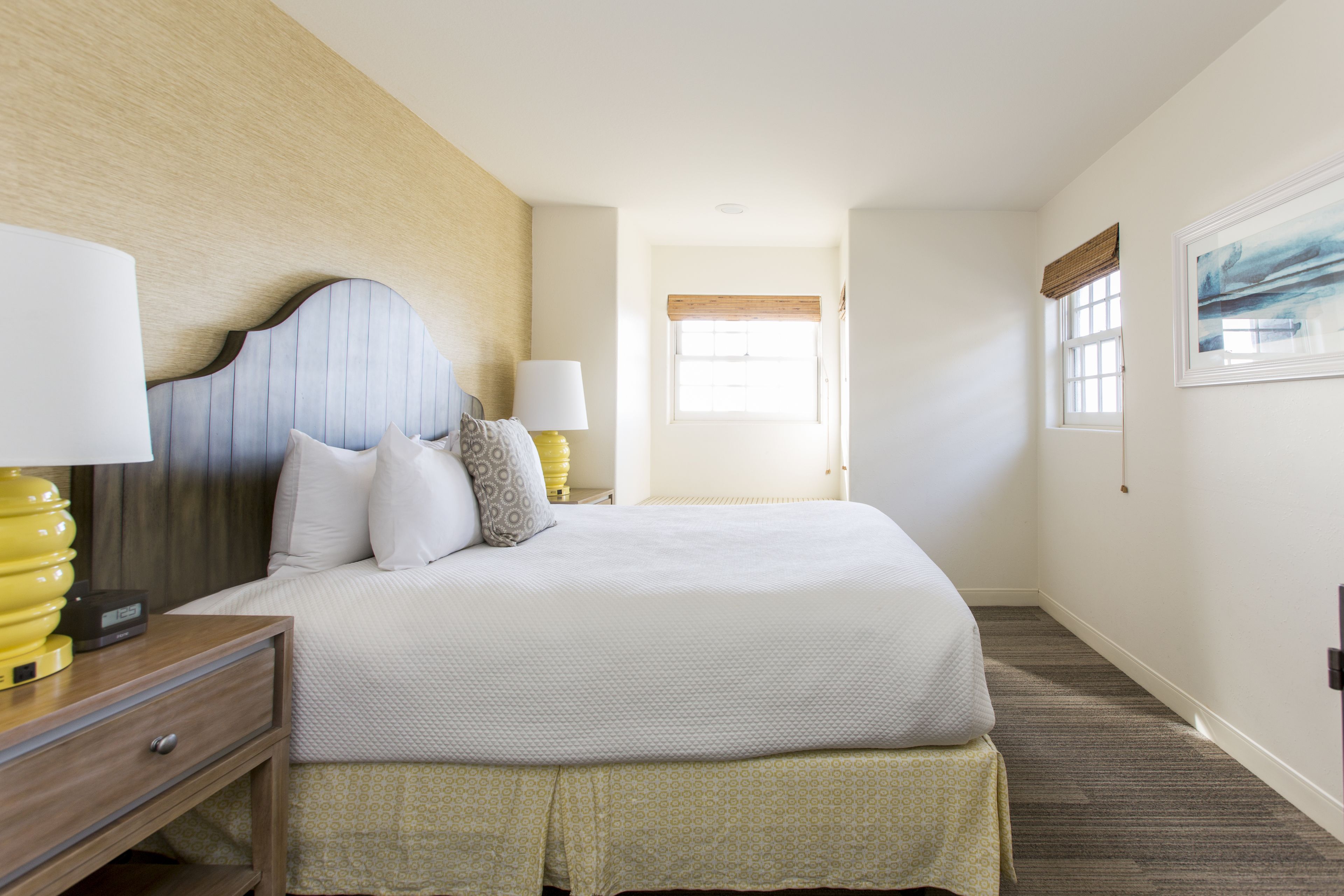 A neatly arranged hotel room with a large bed, bedside lamps, a wooden headboard, and a framed picture on the wall.