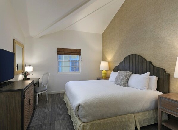A hotel room with a large bed, a desk with a chair, a television, and a window with a view.