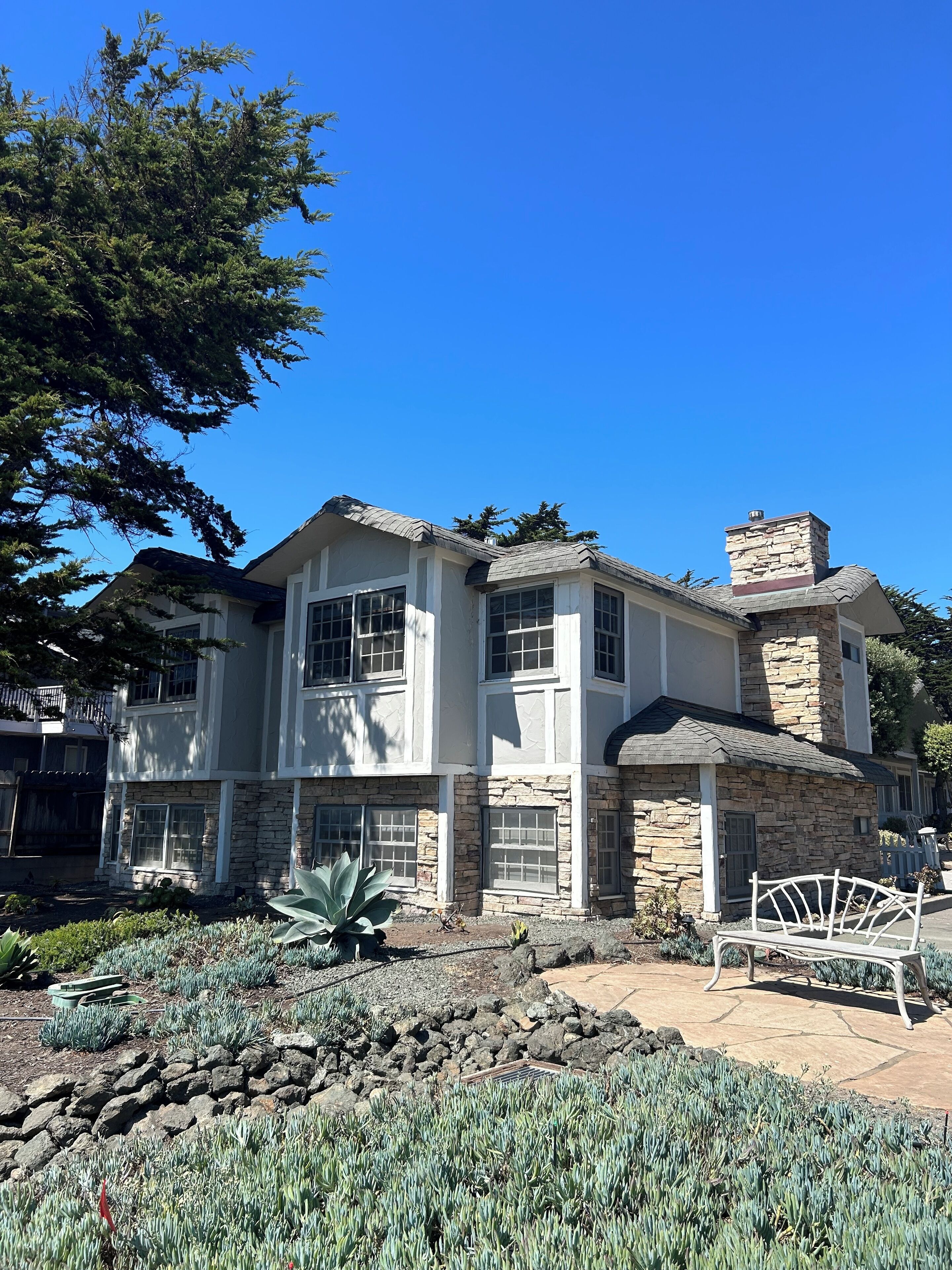 A two-story house with stone and stucco exterior, large windows, and a stone chimney.