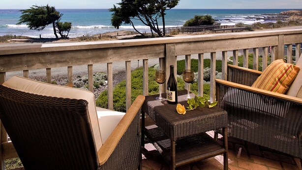 A balcony with wicker furniture, a bottle of wine, and a glass on a table, overlooking the ocean. - FogCatcher Inn (Cambria)