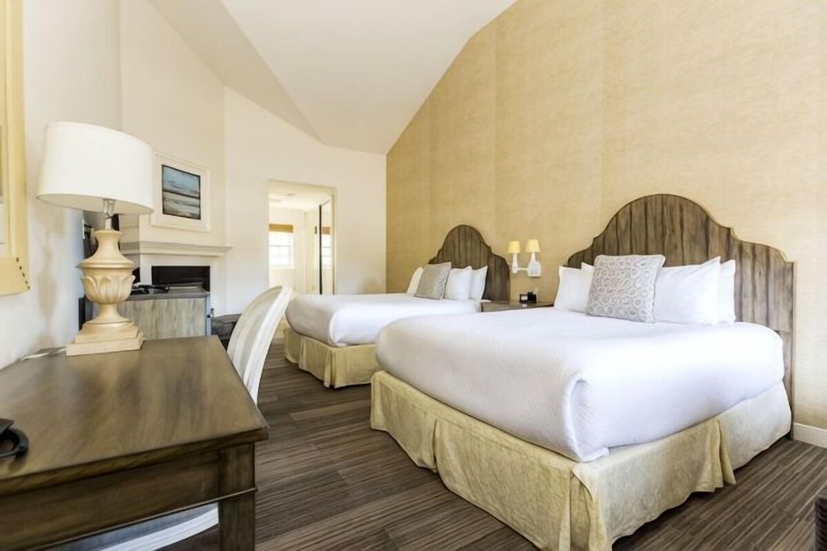 A hotel room with two beds, a desk, and a lamp.