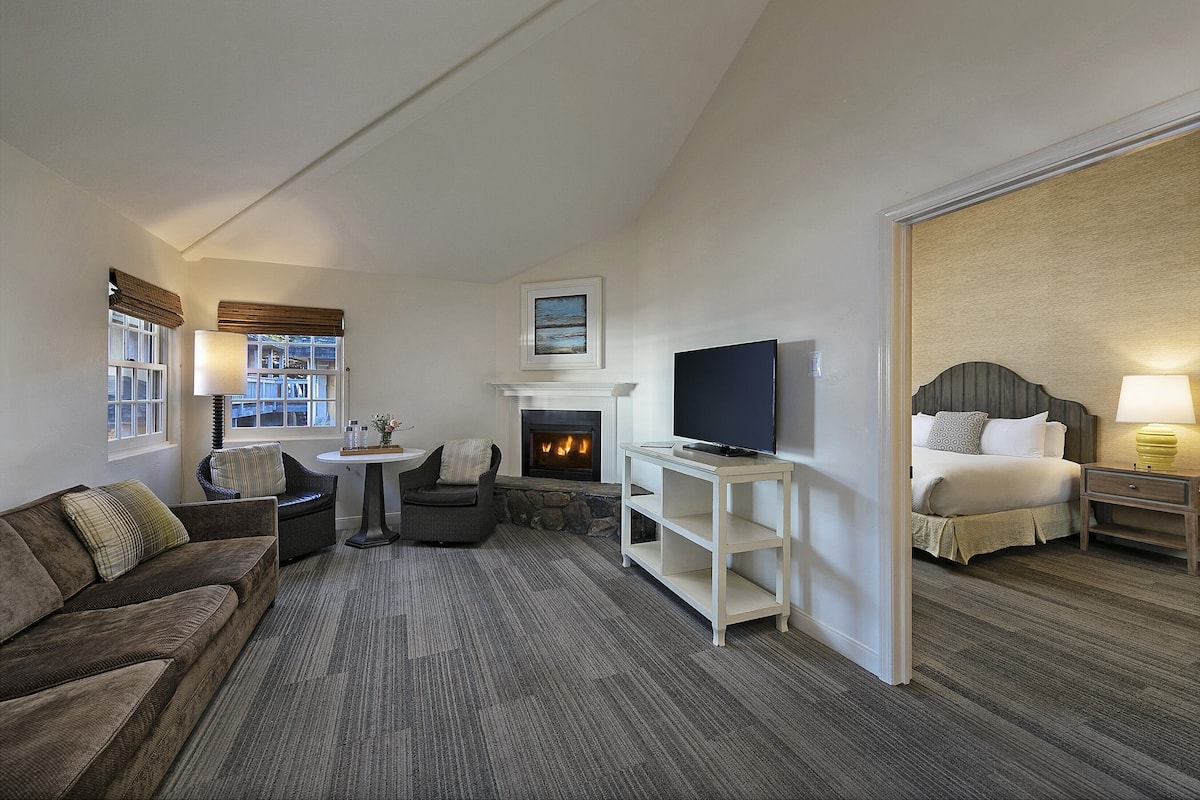 A hotel room with a fireplace, a television, a sofa, a bed, and a small table.