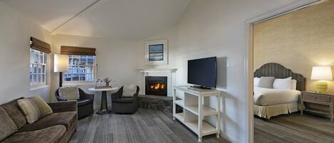 A hotel room with a fireplace, a television, a sofa, a bed, and a small table.