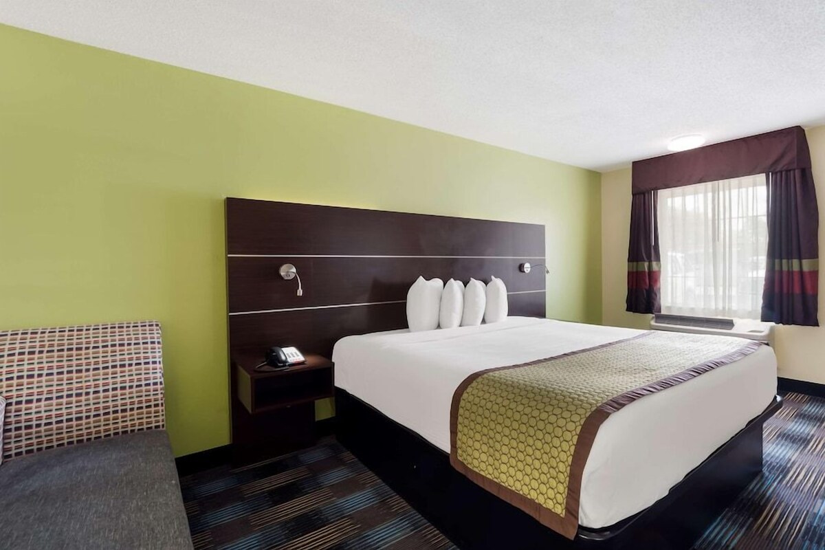 A hotel room with a large bed, a bedside table, a telephone, and a window with curtains.