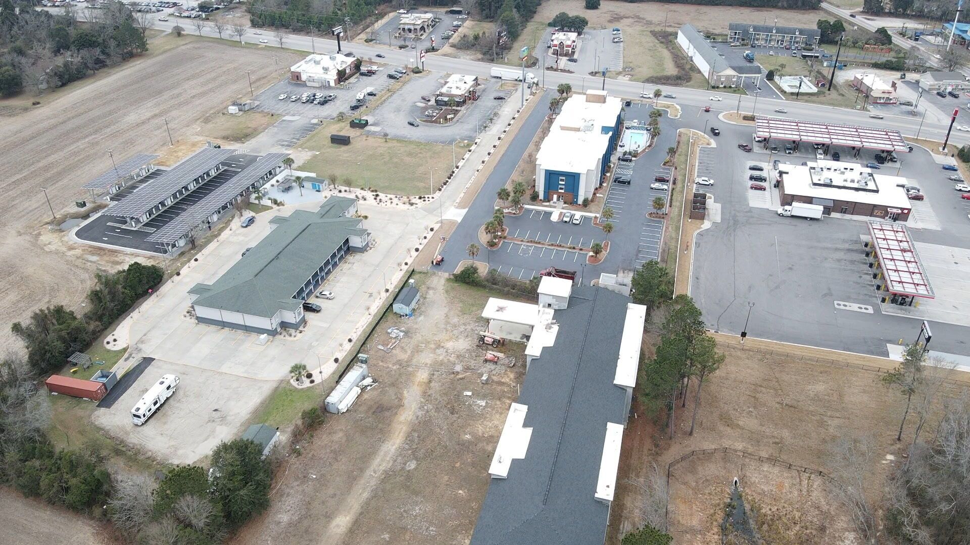 An aerial view of a commercial area with multiple buildings, parking lots, and a large open field.