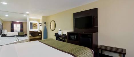 A hotel room with a large bed, a desk with a chair, a microwave, a flat-screen TV, and a small bench.