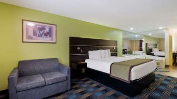 Une chambre d’hôtel avec un lit, un canapé, une table de chevet, un tableau encadré au mur et une salle de bain visible à travers un miroir.