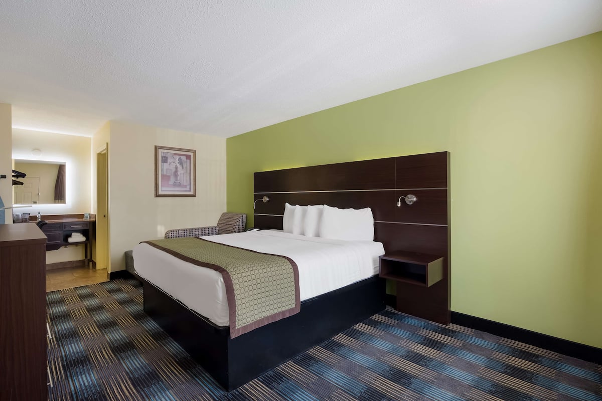A hotel room with a large bed, a desk with a chair, a mirror, and a framed picture on the wall.