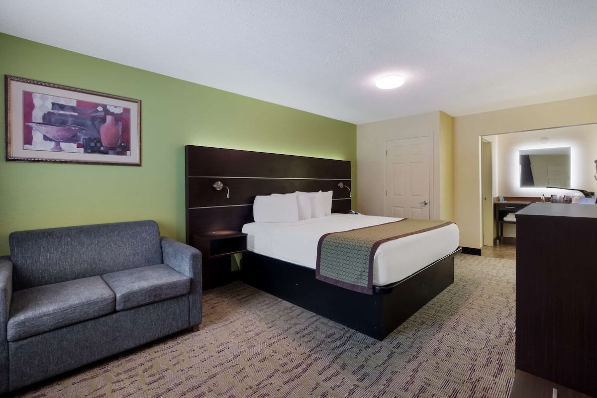 A hotel room with a bed, a couch, a desk, and a bathroom mirror.