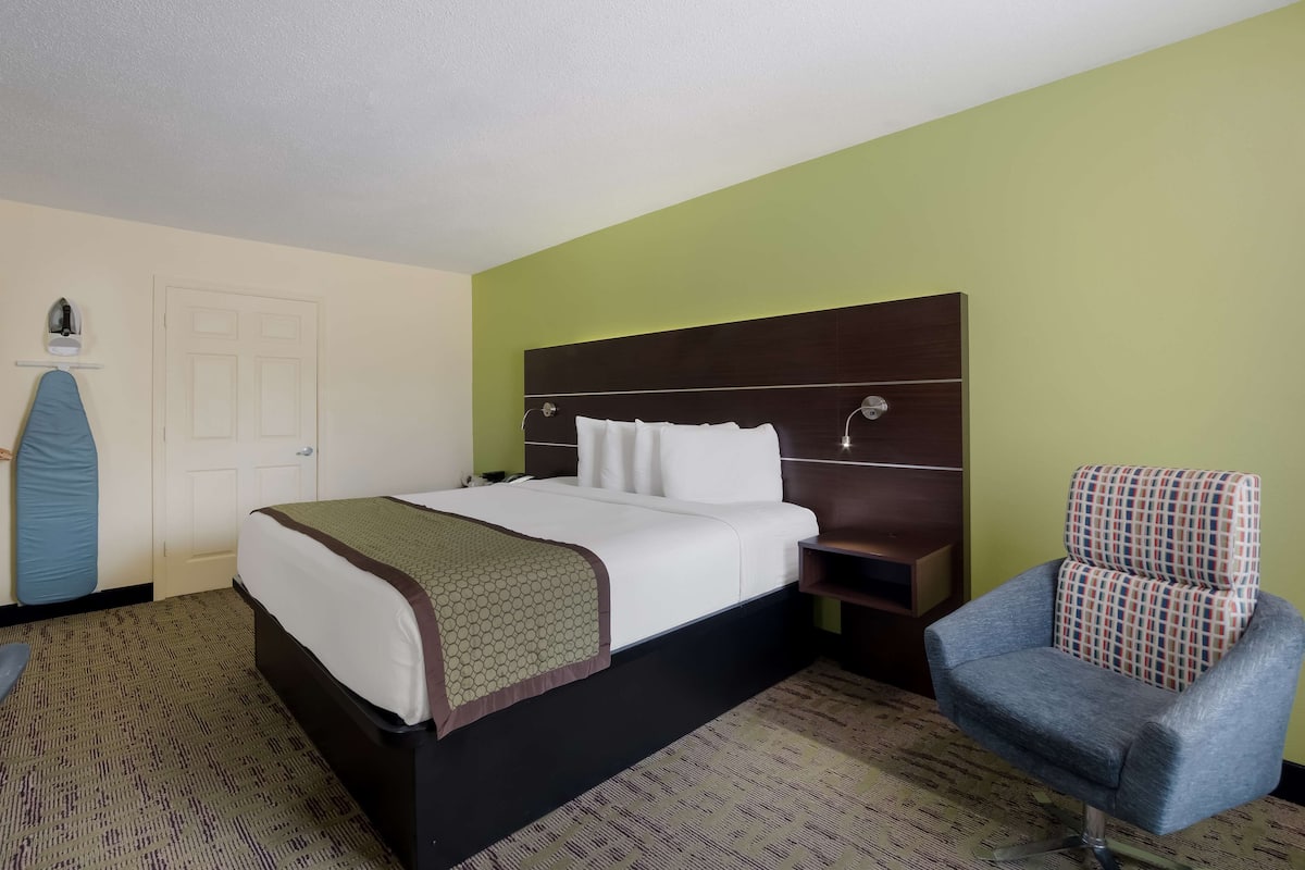 A hotel room with a large bed, a chair, a desk, and a wardrobe.
