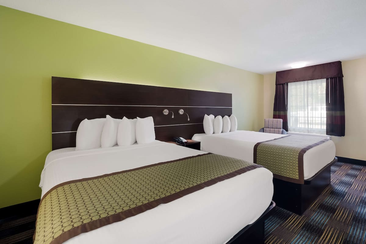 A hotel room with two beds, a large headboard, a telephone, and a window with curtains.