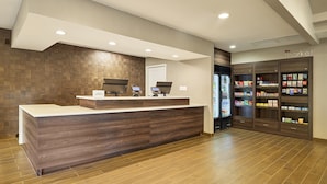 A reception area with a wooden reception desk, a refrigerator stocked with beverages, and a display of snacks and toiletries. - Residence Inn Eugene Springfield (Eugene)