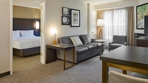 A hotel room with a bed, a grey sofa, a small table, a chair, and a TV. - Residence Inn Eugene Springfield (Eugene)