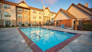A swimming pool with a brick border, surrounded by a paved area and a row of multi-story buildings with a uniform architectural style. - Residence Inn Eugene Springfield (Eugene)