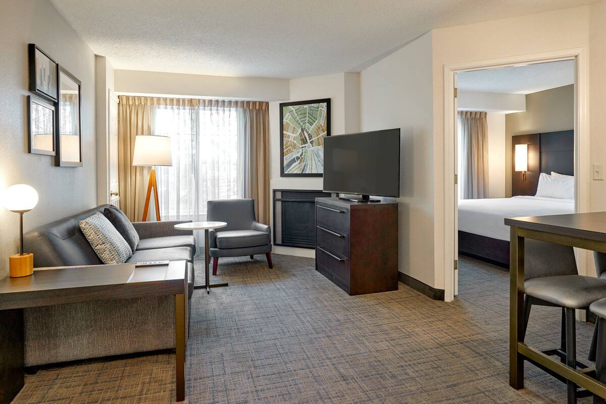 A hotel room with a sofa, armchair, TV, desk, and bed.