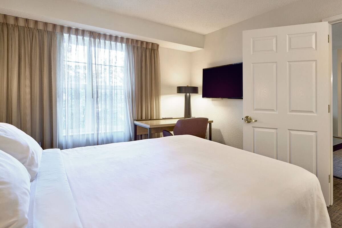 A hotel room with a large bed, a desk, a chair, a television, and a door.