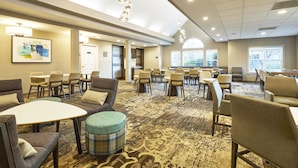 A hotel lobby with a mix of seating options including sofas, chairs, and a round table. There are multiple windows providing natural light and a view of the outdoors. - Residence Inn Eugene Springfield (Eugene)
