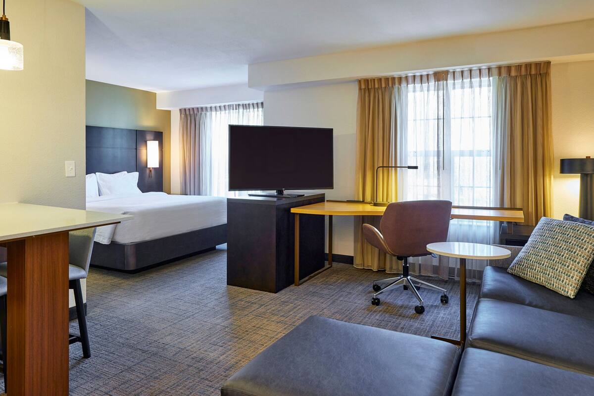 A hotel room with a bed, a desk with a TV, a sofa, and a small table.