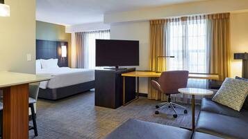 A hotel room with a bed, a desk with a TV, a sofa, and a small table.