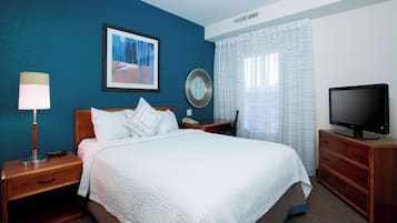 Habitación de hotel con cama, mesita de noche, televisión, lámpara, espejo y ventana con cortinas.