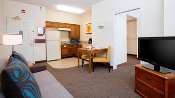 A compact living space with a kitchenette, a dining area, a flat-screen TV, and a sofa with patterned cushions.