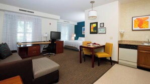 A hotel room with a bed, a desk with a computer, a sofa, a dining table with chairs, a kitchen area with a dishwasher, and artwork on the walls. - Residence Inn by Marriott Olathe Kansas City (Olathe)