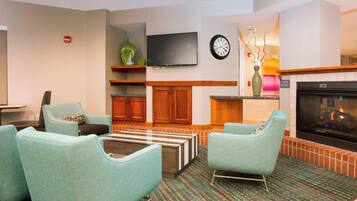 A modern living room with teal armchairs, a flat-screen TV, wooden cabinets, and a fireplace.
