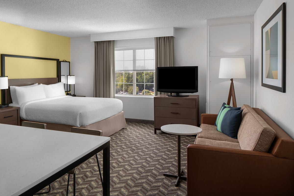 A hotel room with a bed, a TV, a sofa, a desk, and a window with curtains.