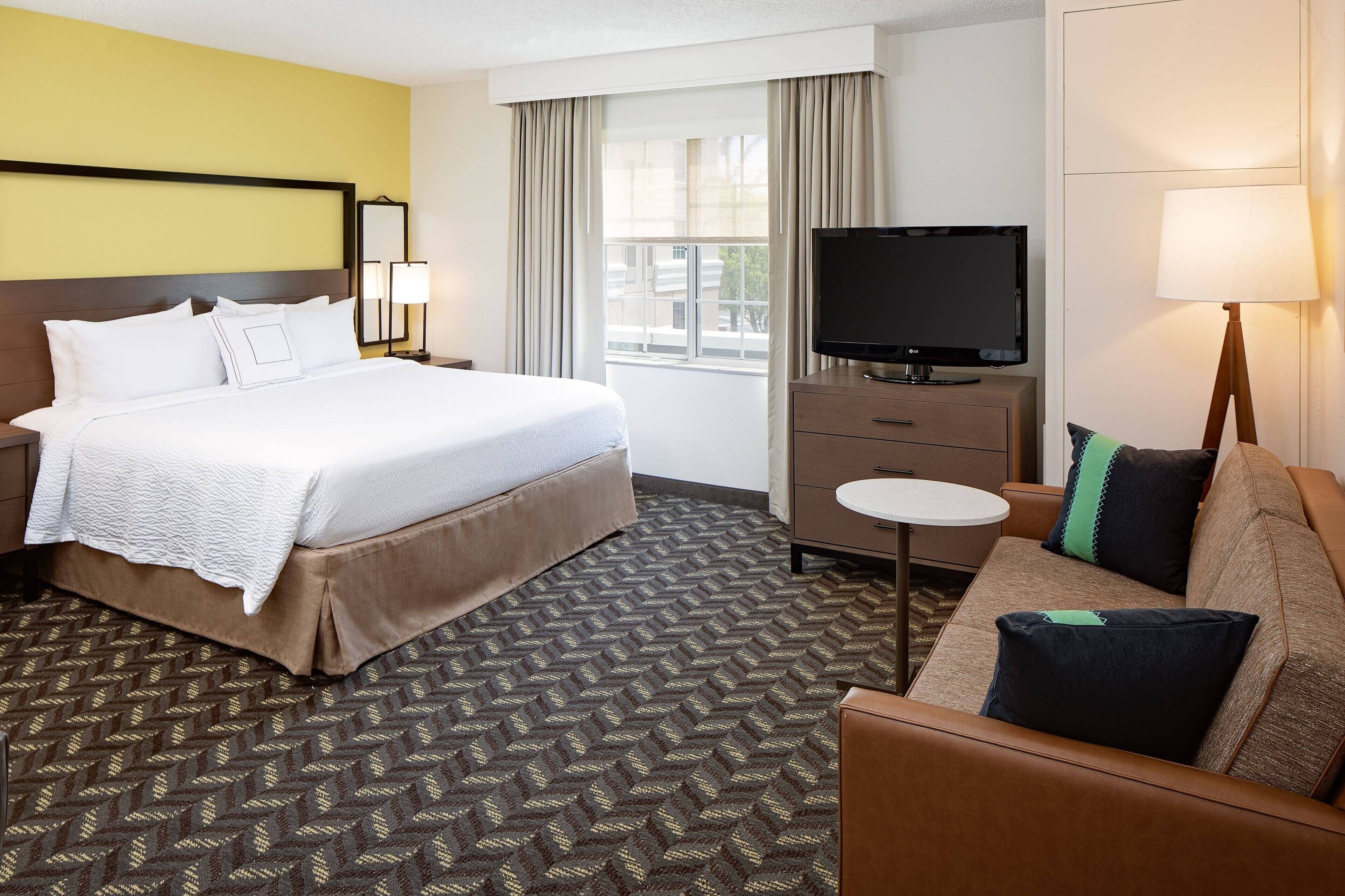 A hotel room with a bed, a TV, a sofa, and a small table.