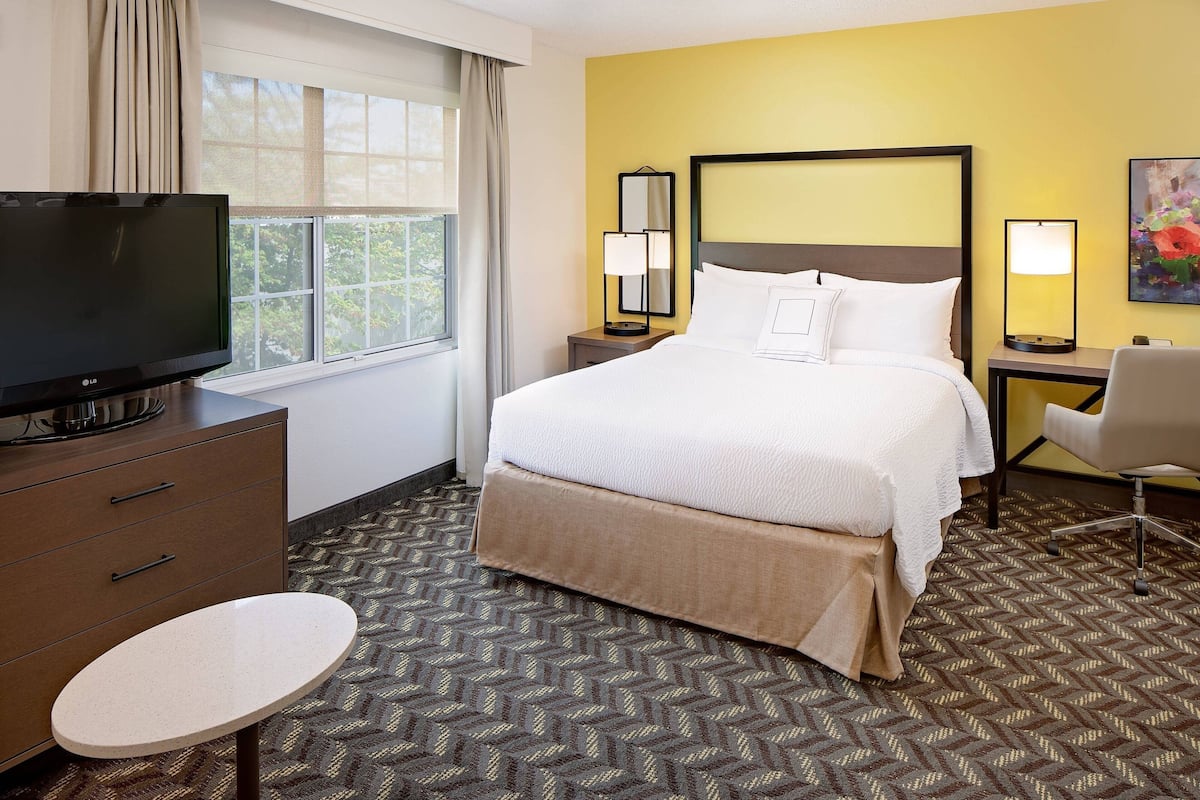 A hotel room with a bed, a TV, a desk, and a chair.