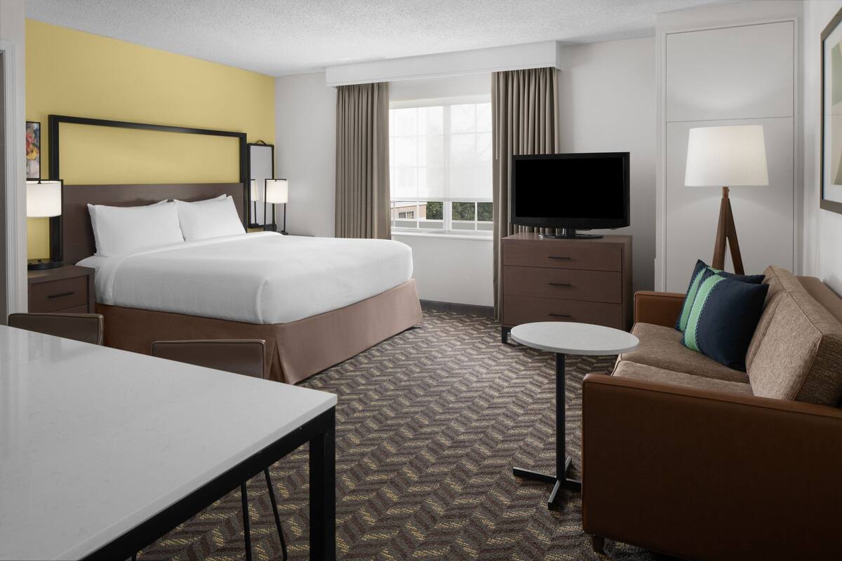 A hotel room with a large bed, a television, a desk, a sofa, and a window with curtains.