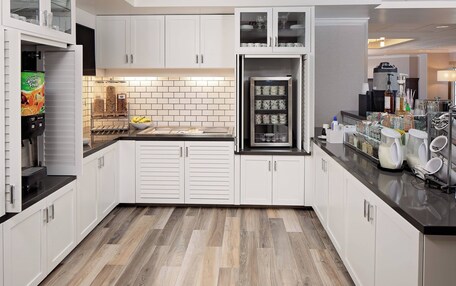 A modern kitchen with white cabinets, a black countertop, and a herringbone wood floor.