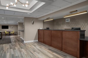 A hotel reception area with a wooden reception desk, a seating area with chairs, and a wall-mounted TV. - Residence Inn by Marriott Tysons (Vienna)
