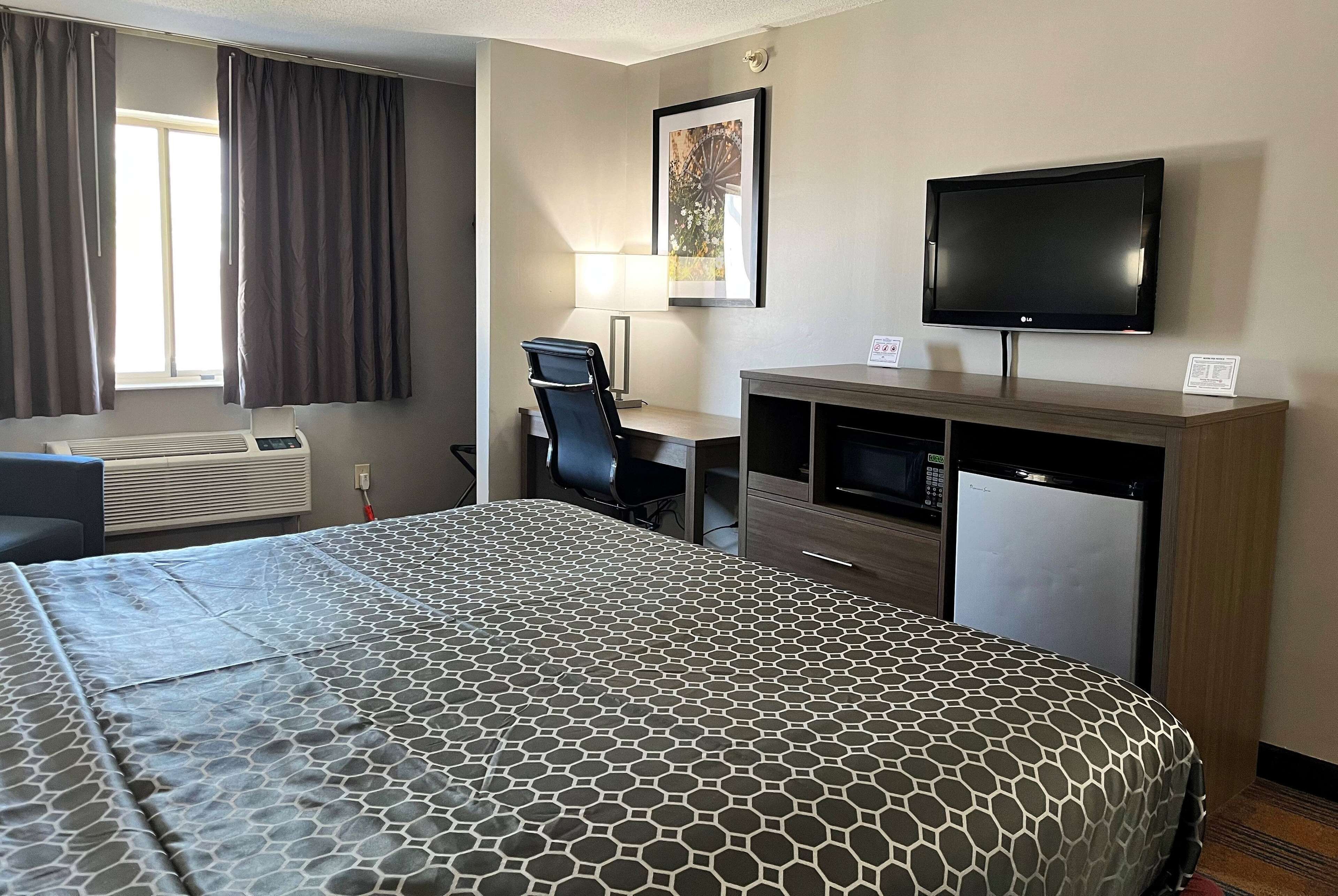 Una habitación de hotel con cama, escritorio, silla, televisor y ventana con cortinas.